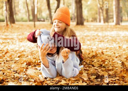 Porträt einer Familie von jungen Frauen und Mädchen im Teenageralter, die im Herbst auf gelben Blättern im Waldpark liegen und Spaß haben. Stockfoto