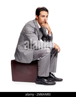 War das die falsche Entscheidung? Ein aufmerksamer junger Geschäftsmann, der auf seiner Aktentasche saß, während er isoliert auf Weiß lag. Stockfoto