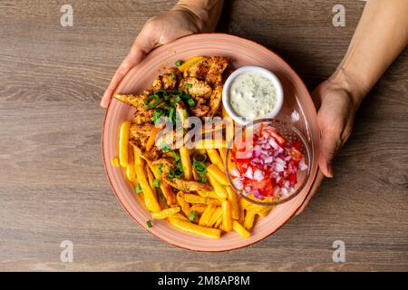 Draufsicht einer unbekannten Frau mit Pommes Frites, gebratenem Hähnchen, geschnittener Tomate mit roten Zwiebeln und weißer Sauce. Stockfoto