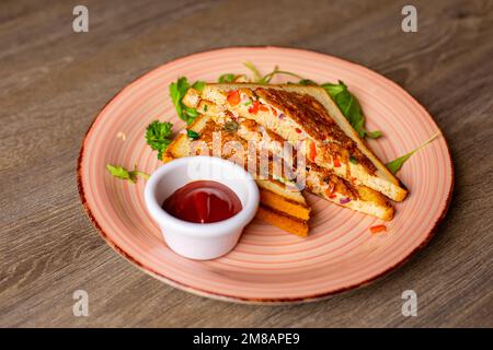 Nahaufnahme eines rosafarbenen Tellers mit leckeren gebratenen Sandwiches, Ketchup in einer kleinen weißen Schüssel, dekoriert mit Grün auf dem Tisch. Stockfoto