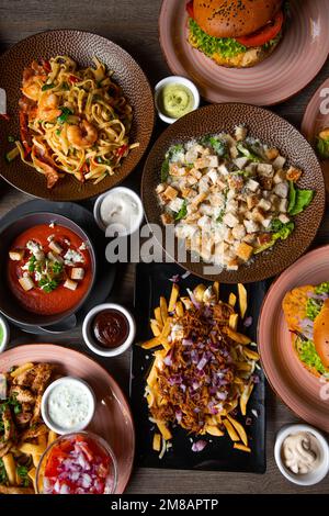 Von oben hat man einen tollen Blick auf das Essen auf einem Holztisch im Restaurant Cafe. Pasta mit Garnelen. Caesar Salat mit Huhn und Croutons. Stockfoto
