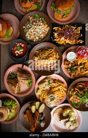 Blick von oben auf leckeres Essen auf dem Tisch im Restaurant. Pasta mit Garnelen. Caesar-Salat. Tomatensuppe. Pommes frites. Burger. Stockfoto