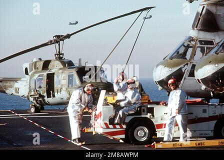 Absturz- und Bergungsmannschaften in Anzügen stehen mit einem MD-3A Feuerwehrfahrzeug während des Flugbetriebs an Bord des Amphibienschiffs USS BELLEAU WOOD (LHA-3) auf dem Cockpit bereit. Marine Medium Helicopter Squadron 161 (HMM-161) CH-46 Sea Knight Helicopters werden im Hintergrund geparkt. Land: Pazifik (POC) Stockfoto