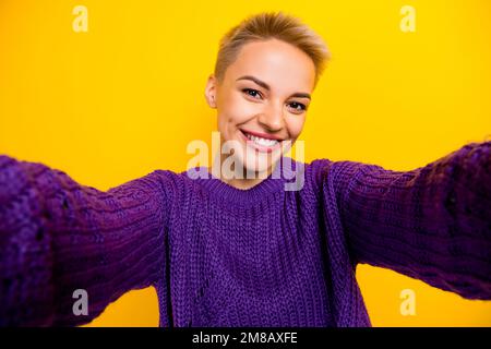 Foto eines zufriedenen, hübschen, netten Mädchens mit kurzer Frisur Strickpullover, der Selfie isoliert auf gelbem Hintergrund macht Stockfoto