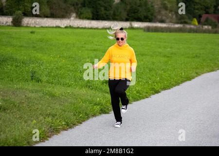 Springen und Laufen blonde Frau in der Natur, um eine ausgewogene Work-Life-Balance zu bekommen und gesund zu werden Stockfoto