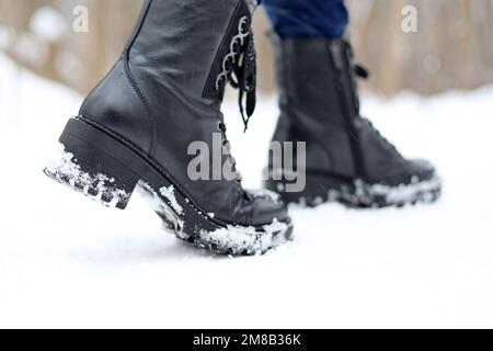 Weibliche Beine in schwarzen Leder Schnürstiefeln auf Schnee. Frau, die auf der Winterstraße läuft, warme Schuhe für kaltes Wetter Stockfoto