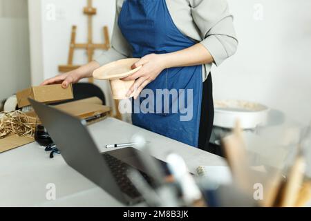 Unbekannte Unternehmerin, Geschäftsinhaberin, die im Heimbüro mit ihrem Tonkeramikprodukt arbeitet. Online-Verkauf geschäftliche Arbeit. Stockfoto