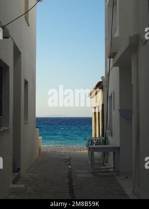 Blick auf das blaue Meer durch eine enge Straße in der Stadt Kokkari. Stockfoto
