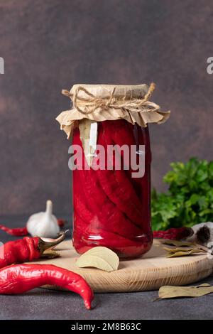 Hausgemachte eingelegte Chilischoten mit Knoblauch im Glas auf Holzbrett Stockfoto