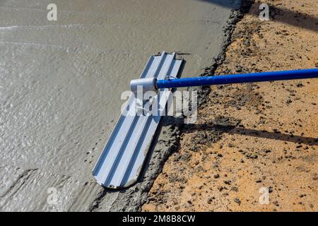 Während der Arbeiter die Stahlkelle fresno im Baubereich hält, glättet er den neuen Bürgersteig auf nassem Beton, der gerade ausgegossen wurde. Stockfoto