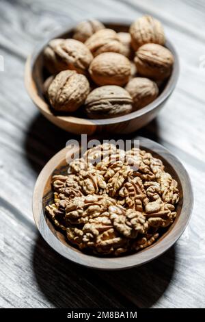 Geschälte Walnüsse und Nüsse in einer Schale in einer Holzschüssel aus Walnuss auf einem Holzhintergrund. Nüsse und gesundes Essen Konzept. Vertikaler Schuss. Stockfoto