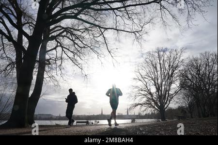 Hamburg, Deutschland. 13. Januar 2023. Ein Jogger läuft im Sonnenschein entlang der Außenalster. Kredit: Marcus Brandt/dpa/Alamy Live News Stockfoto