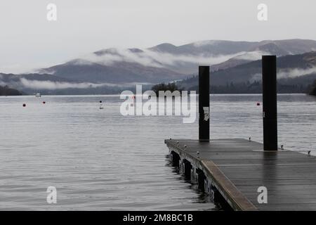 Anlegestelle am Lake Windermere mit Nebel über den Bergen an einem bewölkten Tag Stockfoto