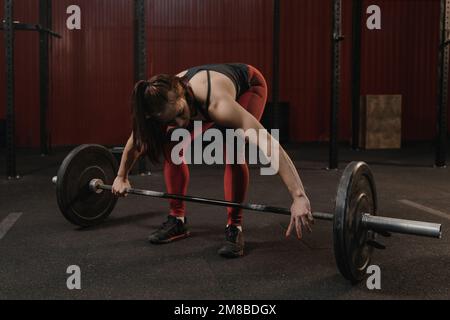 Junge Crossfit-Frau, die die Hantel für das Gewichtheben im Fitnessstudio vorbereitet. Sportlerin, die funktionelles Training macht. Stockfoto