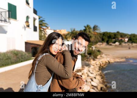Seitenansicht der jungen Brünette, die während eines romantischen Dates am Valentinstag auf dem Meer mit einem Lächeln in die Kamera schaut Stockfoto