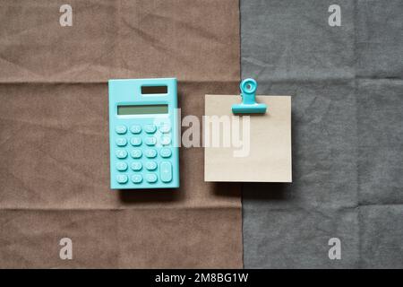 Minzrechner und Notizblock auf braunem und grauem Stoffhintergrund. Draufsicht, Kopierbereich Stockfoto