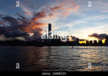 Die Sonne geht über Kowloon in Hongkong auf. Meer im Vordergrund. Gebäude in Silhouette. Stockfoto