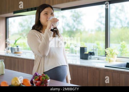 Charmante asiatische Schwangere, die Milch aus Glas trinkt. Attraktive Frau braucht Protein und Kalzium für ihr Baby und es macht sie gesund und stark. Stockfoto