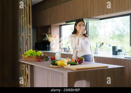 Charmante asiatische Schwangere, die Milch aus Glas trinkt. Attraktive Frau braucht Protein und Kalzium für ihr Baby und es macht sie gesund und stark. Stockfoto