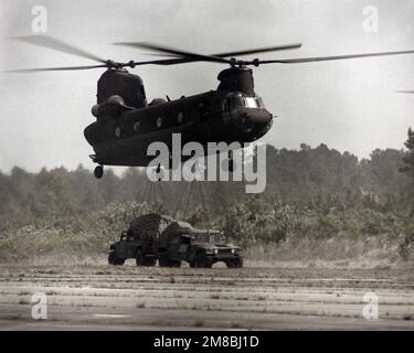 Ein Army CH-47 Chinook Helikopter bringt ein Paar M998 High-Mobility Multipurpose Wheeled Vehicles (HMMWV) in einer Landezone während der gemeinsamen Serviceübung SOLID SHIELD '89 ab. Betreff Operation/Serie: SOLID SHIELD '89 Basis: Camp Davis Bundesstaat: North Carolina (NC) Land: Vereinigte Staaten von Amerika (USA) Stockfoto