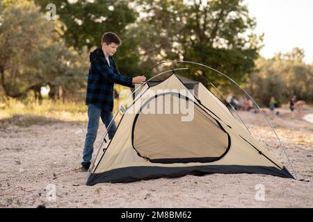 Ein Teenager-Junge baut das Zelt auf dem Campingplatz an einem Sommertag auf, ein Junge campen mit Zelt, Kopierraum Stockfoto