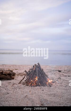 Lagerfeuer am Strand bei Sonnenuntergang. Feuer am Strand. Einladendes Lagerfeuer am Strand im Sommer. Einsames Feuer am Meer. Spaß und Erinnerungen im Stockfoto