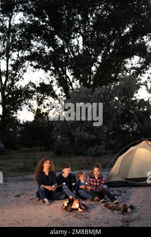 Glückliche Familienmutter und Kinder, die Marshmallows über dem Feuer in einem Grill im Camp rösten Stockfoto