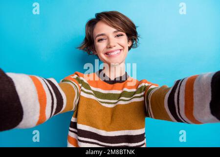 Foto einer optimistisch positiven, hinreißenden Frau mit kurzer Frisur und gestreiftem Pullover, die Selfie isoliert auf blauem Hintergrund macht Stockfoto