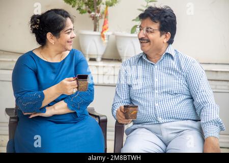Glückliches indisches, reifes Paar, das morgens Tee oder Kaffee genießt und sich unterhält. Privat- oder Ruhestandsleben. Stockfoto