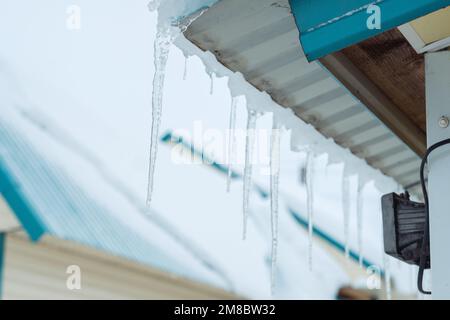 Eiszapfen hängen auf dem Dach. Gefahr im Winter Stockfoto