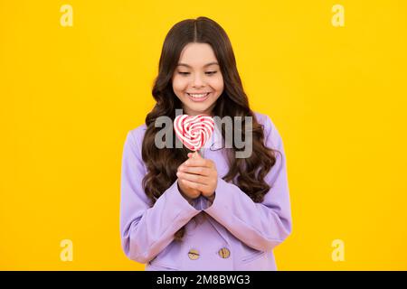 Lustiges Kind mit Lutscher auf gelbem isoliertem Hintergrund. Süßes Kindheitsleben. Teen Mädchen mit yummy Karamell Lollipop, Süßwarenladen. Glücklicher Teenager Stockfoto