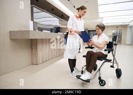 Der Arzt kommuniziert mit einer älteren Frau im Rollstuhl an der Rezeption Stockfoto