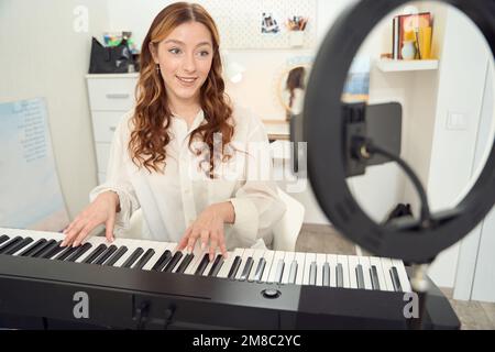 Ein fröhlicher Synthesizer-Spieler streamt ihre Leistung live an das Publikum Stockfoto