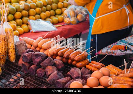 Thailändische Würstchen auf einem Stock und Gemüse, die von einem Street Food-Verkäufer und Obstverkäufer am Doi Kio Lom ViewPoint im Norden Thailands gegrillt werden. Stockfoto