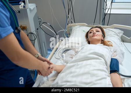 Hübsche Frau liegt auf der Intensivstation und schaut auf Krankenschwester Stockfoto