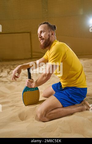 Der Sportler sitzt auf Sand und hält einen Schläger in der Hand Stockfoto