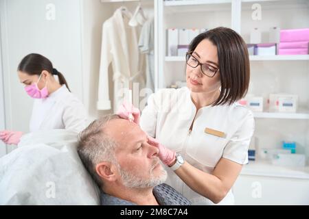 Kosmetiker macht Markierungen auf der Stirn eines Mannes Stockfoto