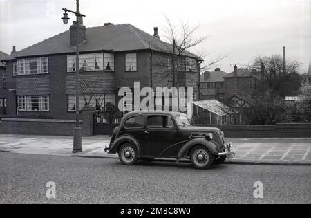 1950er, historisch, ein Auto der Epoche, ein Ford Anglia, geparkt in einer Straße von Vorstadthäusern in Didsbury, Manchester, England, Großbritannien. Stockfoto