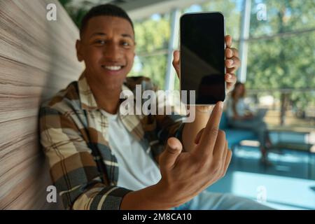 Ein glücklicher afroamerikanischer Typ, der mit dem Finger auf den Handy-Bildschirm zeigt Stockfoto