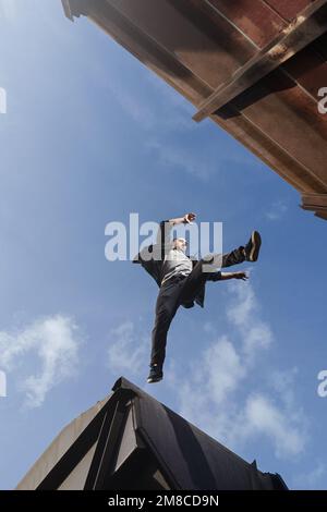 Ein Mann, der gruselig zwischen den Dächern springt. Ein Typ, der Parkour-Freerunning praktiziert. Stockfoto