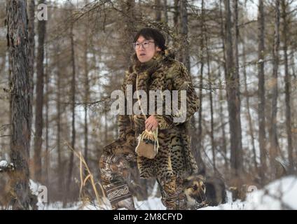 (230113) -- GENHE, 13. Januar 2023 (Xinhua) -- Juele sucht nach seinem Rentier im Jinhe Forest Range nahe Genhe City, Nordchina's innere Mongolei Autonome Region, 12. Januar 2023. Alle zwei oder drei Tage fährt Juele Bulituotian zum Jinhe-Waldgebiet etwa 80 Kilometer von Genhe City entfernt. Dort wird der 39-jährige Aoluguya Ewenki-Hirte, der einen traditionellen Pelzmantel trägt, sein forschendes Rentier finden. Anstatt Rentiere in einer Scheune zu halten, lassen die Ewenki-Hirten die Tiere im Wald leben und überprüfen sie alle paar Tage. Juele besitzt über 60 Rentiere. Er wird seine Zügel rufen Stockfoto
