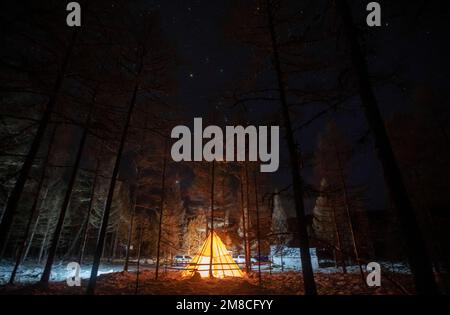 (230113) -- GENHE, 13. Januar 2023 (Xinhua) -- Dieses Foto wurde am 11. Januar 2023 aufgenommen und zeigt ein traditionelles Ewenki-Zelt in einer temporären Herdstation in der Jinhe-Waldkette in der Nähe der Stadt Genhe, Nordchina Autonome Region der inneren Mongolei. Alle zwei oder drei Tage fährt Juele Bulituotian zum Jinhe-Waldgebiet etwa 80 Kilometer von Genhe City entfernt. Dort wird der 39-jährige Aoluguya Ewenki-Hirte, der einen traditionellen Pelzmantel trägt, sein forschendes Rentier finden. Anstatt Rentiere in einer Scheune zu halten, lassen die Ewenki-Hirten die Tiere im Wald leben und überprüfen sie alle paar Tage. Stockfoto