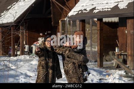 (230113) -- GENHE, 13. Jan. 2023 (Xinhua) -- Dieses Foto wurde am 13. Jan. 2023 aufgenommen und zeigt Juele mit seiner Familie in einer neuen Umzugsgemeinde in Aoluguya Ewenki, Genhe City in Nordchinas Autonomer Region der inneren Mongolei. Alle zwei oder drei Tage fährt Juele Bulituotian zum Jinhe-Waldgebiet etwa 80 Kilometer von Genhe City entfernt. Dort wird der 39-jährige Aoluguya Ewenki-Hirte, der einen traditionellen Pelzmantel trägt, sein forschendes Rentier finden. Anstatt Rentiere in einer Scheune zu halten, lassen die Ewenki-Hirten die Tiere im Wald leben und überprüfen sie alle paar Tage. Ju Stockfoto