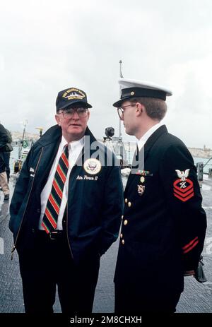 Ein leitender Petty Officer spricht mit einem Mitglied der Präsidentschaftspartei auf dem Deck des geführten Raketenkreuzers USS BELKNAP (CG 26). Präsident George H.W. Bush besucht das Flaggschiff der Sechsten Flotte vor seinem Gipfeltreffen im Dezember 2-3 mit dem sowjetischen Vorsitzenden Michail Gorbatschow. Basis: Marsaxlokk Bay Country: Malta (MLT) Stockfoto