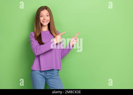 Foto eines Mädchens mit glatter Frisur und violettem Sweatshirt, das den leeren Raum isoliert auf grünem Hintergrund lenkt Stockfoto