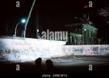 Die ostdeutschen Wachen beobachten, wie sich ein Kran darauf vorbereitet, einen Abschnitt der Berliner Mauer neben dem Brandenburger Tor zu entfernen. Basis: Berlin Land: Deutschland / Deutschland (DEU) Stockfoto