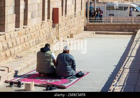 LUXOR, ÄGYPTEN - 27. Dez. 2022. Unwiedererkennbarer muslimischer, arabischer, ägyptischer Vater und Sohn, der in einer Touristenattraktion auf einem Teppich kniete Stockfoto