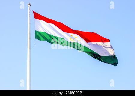 Die nationale rote, weiße und grüne Flagge Tadschikistans auf dem Fahnenmast vor dem blauen Himmel. Stockfoto