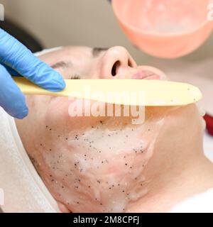 Das Verfahren zum Auftragen einer feuchtigkeitsspendenden Maske auf das Gesicht in einem Spa-Salon, das Auftragen der Maske mit einem Spachtel. Stockfoto