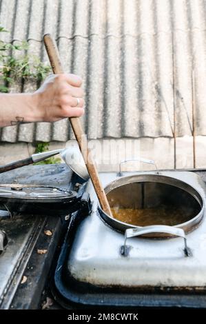 Ein Mann bereitet das Mittagessen in einer Militärküche zu, einem großen Holzspachtel zum Rühren von Essen. Stockfoto